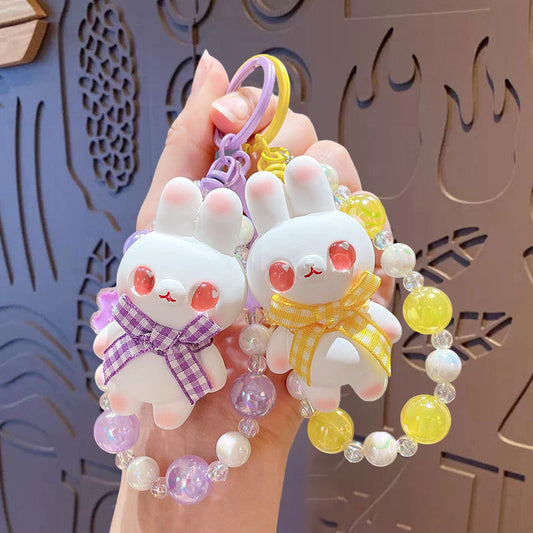 Set of four cute rabbit-shaped keychains with colorful beads on a hand against a decorative background.