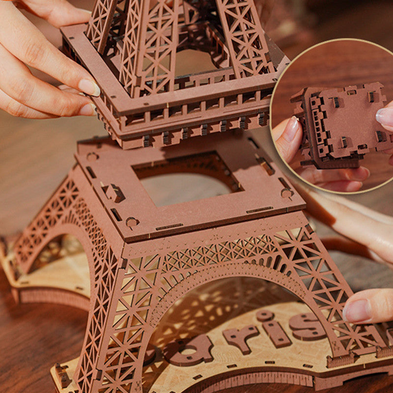 Wooden Eiffel Tower model being assembled with a close-up of hands and puzzle piece.