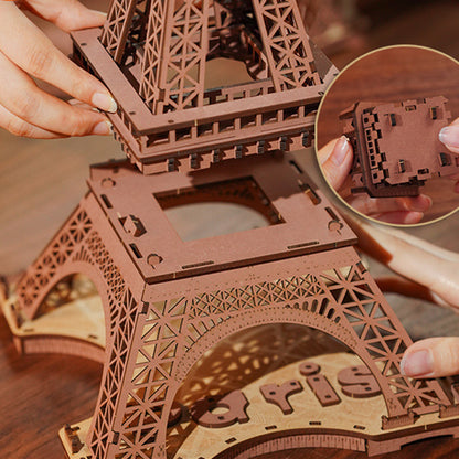 Wooden Eiffel Tower model being assembled with a close-up of hands and puzzle piece.