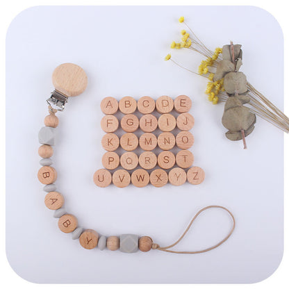 Wooden pacifier clip with letter beads and a small plant on a light background