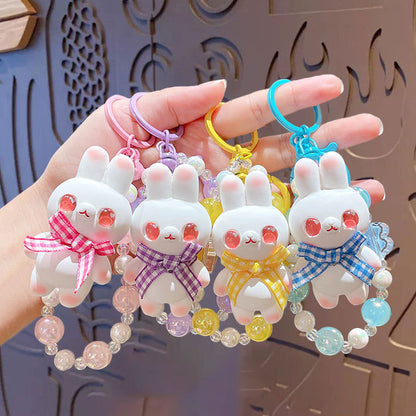 Set of four cute rabbit-shaped keychains with colorful beads on a hand against a decorative background.