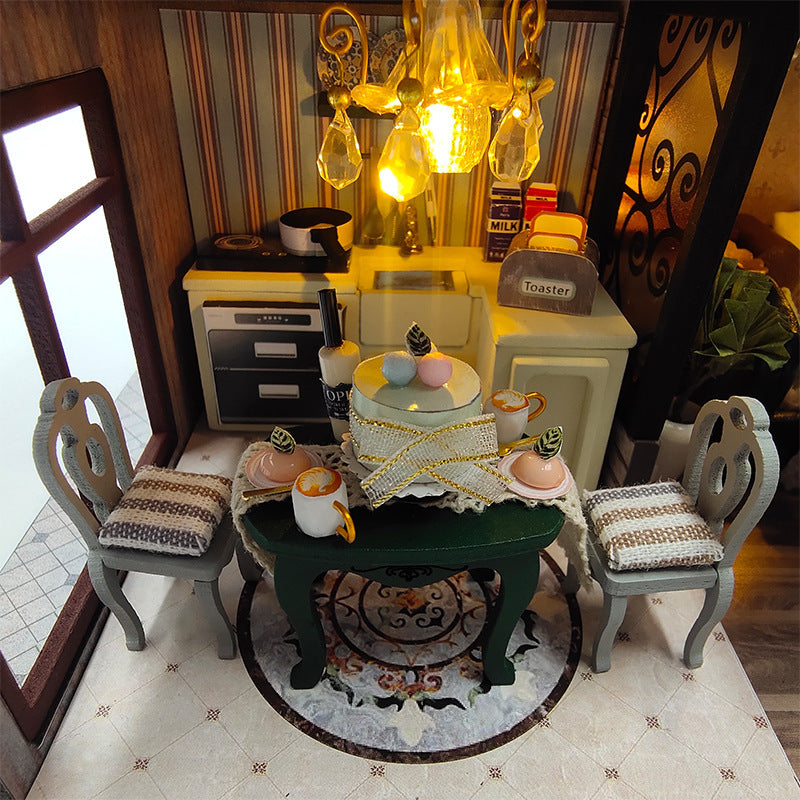 Miniature kitchen setup with table, chairs, and decorative items in a dollhouse.