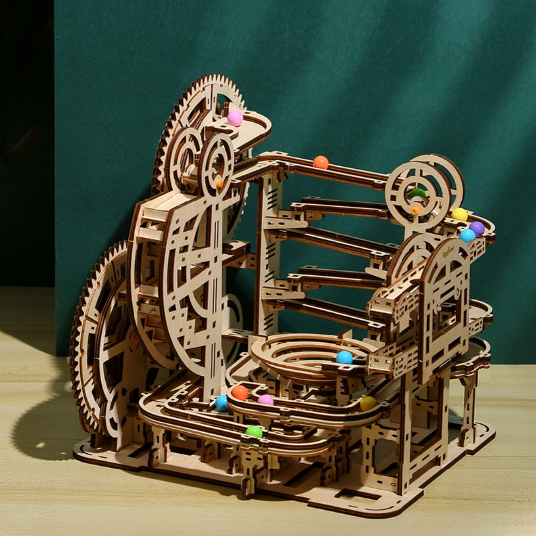 Wooden mechanical model with gears and colorful balls on a wooden surface and green background