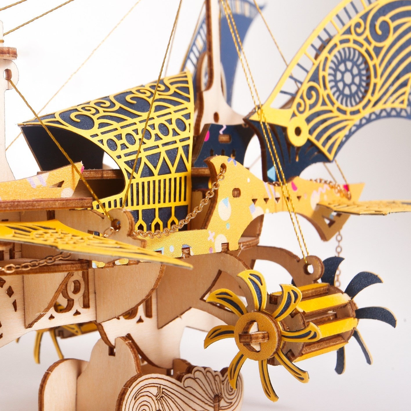 Close-up of a detailed wooden model ship with gold and blue accents on a white background